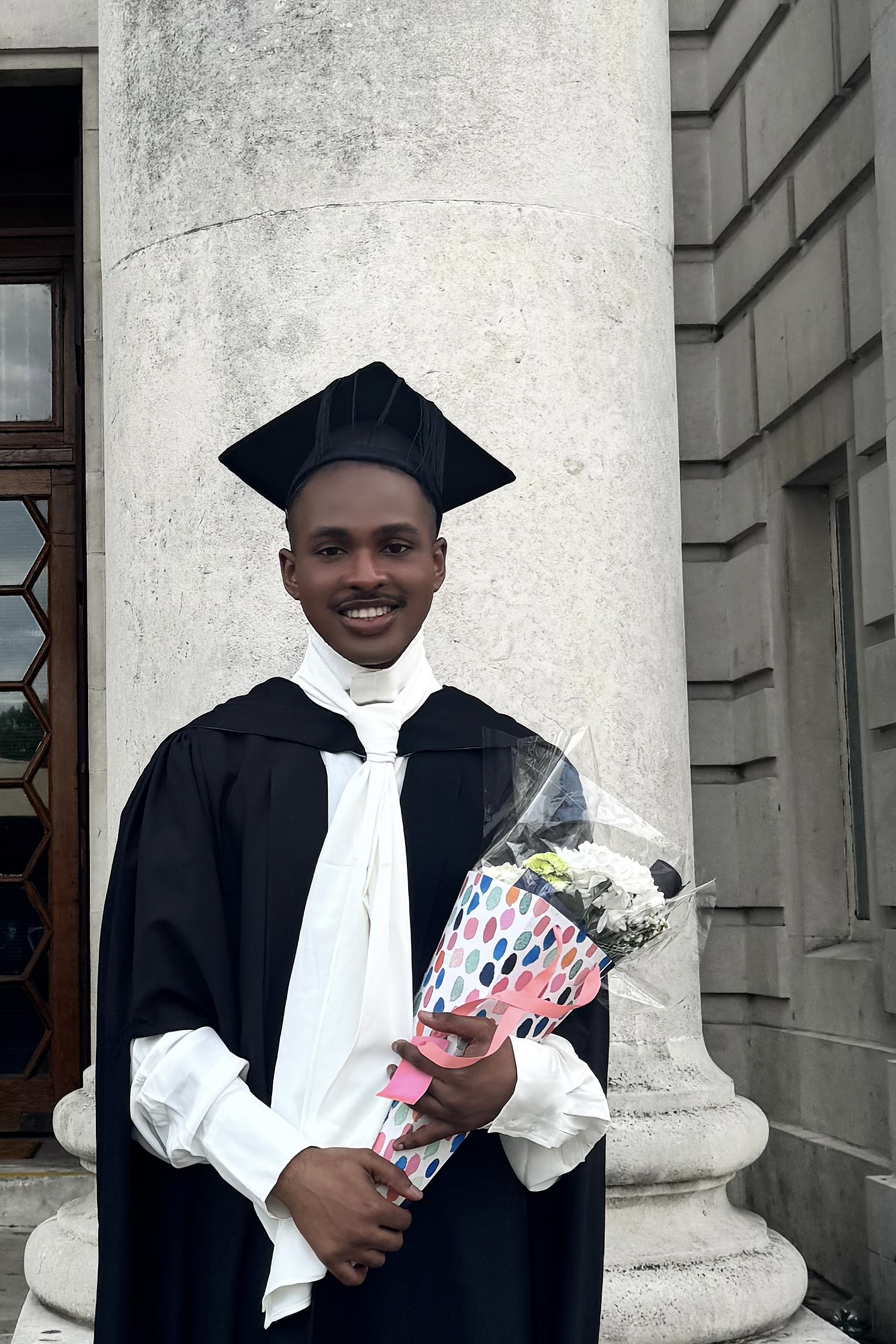 Orasiki Wellington in graduation attire holding flowers